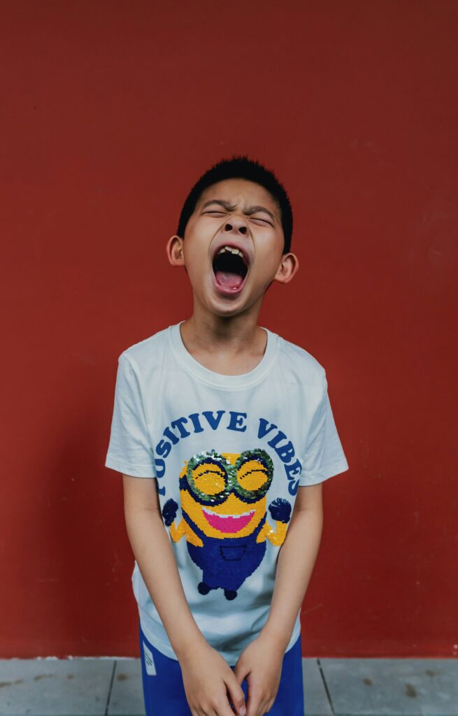 Young boy looking up and shouting, wearing a t-shirt that says positive vibes with a minion smiling. 